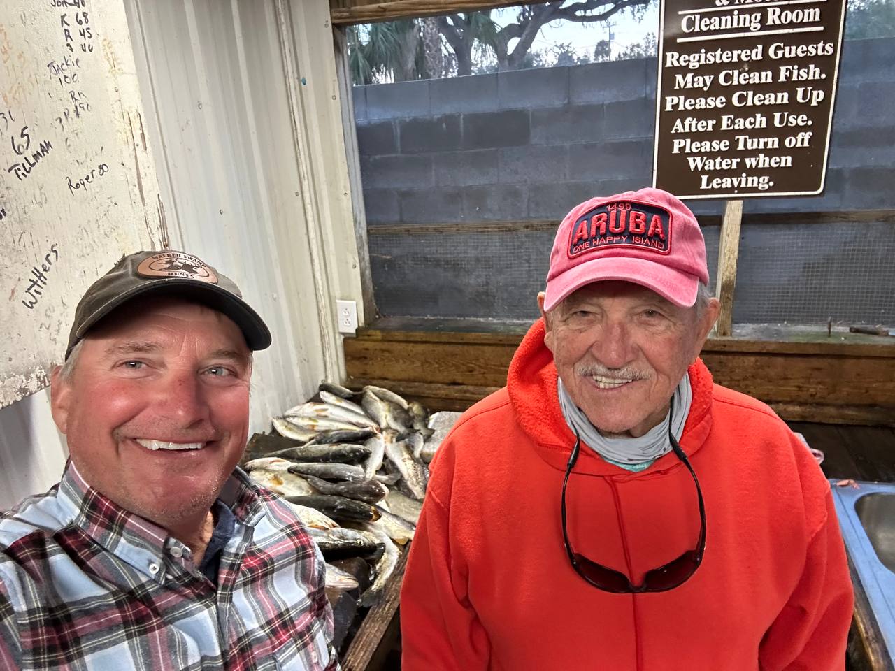 Two fishermen smiling in a cleaning room with fish behind them